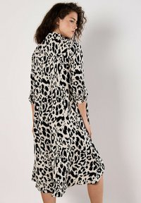 Leopardenmuster Kleid in Creme und Schwarz, aus weichem Stoff, mit einer lässigen Silhouette, Knopfkragen und hochgekrempelten Ärmeln.