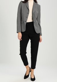 Svart och vit houndstooth-blazer med två knappar, tillsammans med åtsittande svarta byxor och svarta spetsiga klackar. Gräddfärgad polotröja under.