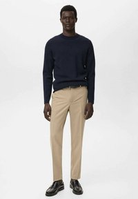 Jersey de punto azul marino, pantalones beiges y mocasines negros. Diseño sencillo con cuello redondo y corte entallado. Textura suave, estilo informal.