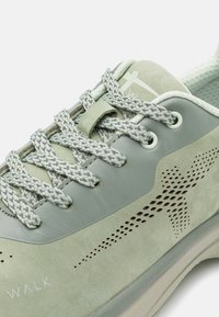 Světle zelené tenisky s kombinací hladkých a semišových textur, perforovanými detaily a šedými vzorovanými tkaničkami. Na boku je nápis "WALK".