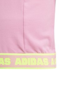 Ροζ αθλητική μπλούζα με ραβδωτή υφή, χαρακτηρισμένη από μια φωσφορούσα κίτρινη λωρίδα λογότυπου στο στρίφωμα. Ο σχεδιασμός τονίζει μια εφαρμοστή σιλουέτα.