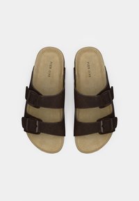 Καφέ σουέτ σανδάλια με δύο ρυθμιζόμενους ιμάντες με αγκράφες και μπεζ εσωτερική σόλα. Επίπεδη σόλα με στρογγυλεμένο σχέδιο στα δάχτυλα.