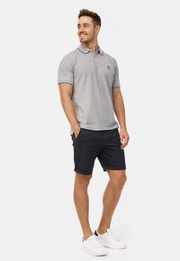 Šedé polo tričko s kontrastním límcem, spárované s námořnickými šortkami. Model má na sobě bílé tenisky. Jednoduchý design, krátké rukávy a volný střih.