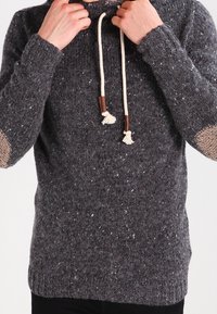 Grauer Strickpullover mit gesprenkelter Textur, ausgestattet mit einer Kapuze, beigen Ellbogen-Patches und cremefarbenen Kordeln mit Holzakzenten.