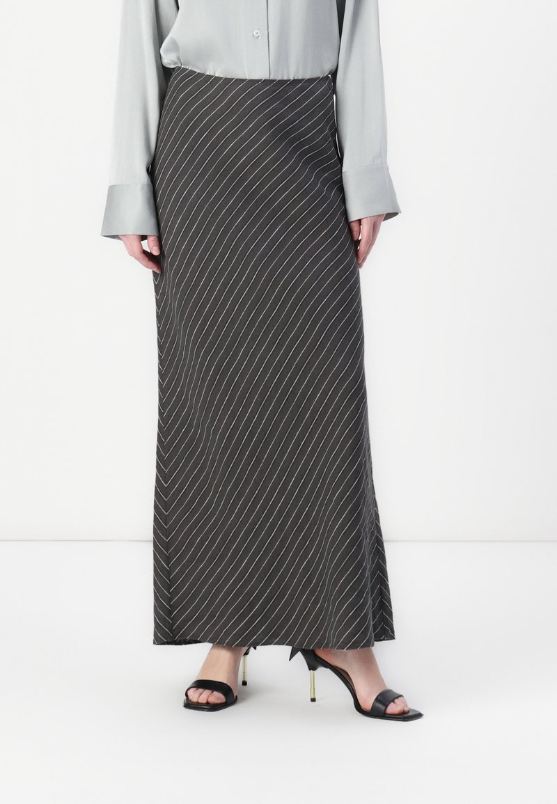 Maxi skirt in dark gray with white diagonal stripes, made of a smooth fabric. Paired with a light gray blouse and black strappy heels.