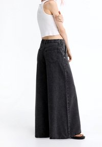 Pantalones de mezclilla negros de pierna ancha con cintura elástica, que cuentan con dos bolsillos traseros y una textura descolorida. Combinados con un top corto blanco.