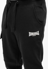 Svarta sweatpants i bomullsblandning med elastisk midja, dragsko, sidofickor och vitt broderat logo "Lonsdale London" på låret.