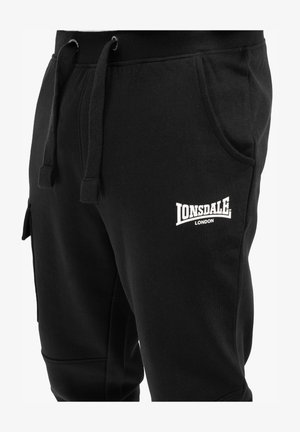 Fekete pamut keverék kapucnis nadrág, elasztikus derékrésszel, húzózsinórral, oldalsó zsebekkel és fehér hímzett "Lonsdale London" logóval a combon.