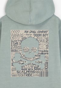 Lyseblå hoodie med en cremefarvet rektangulær grafik, sort tekst og et centralt kraniedesign, der fremhæver urban temaer og slogans.