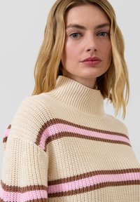 Beżowy dzianinowy sweter z wysokim kołnierzem i poziomymi paskami w kolorze różowym i brązowym. Tkanina o fakturze, zapewniająca przytulny wygląd, z luźnym krojem.