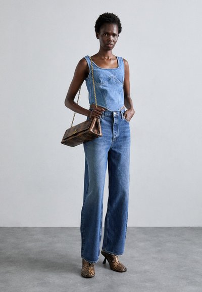 Denim top with square neckline and light blue jeans; brown snakeskin-patterned heeled boots; metallic-accented handbag with chain strap.