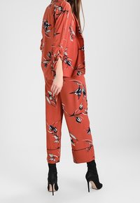 Červeno květinový dvoudílný outfit s černými a bílými akcenty. Halenka má dlouhé rukávy, zatímco kalhoty mají volný střih, doplněné černými podpatky.