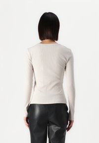 Light beige long-sleeve top made of ribbed fabric, featuring a rounded neckline and fitted design, paired with black leather pants.