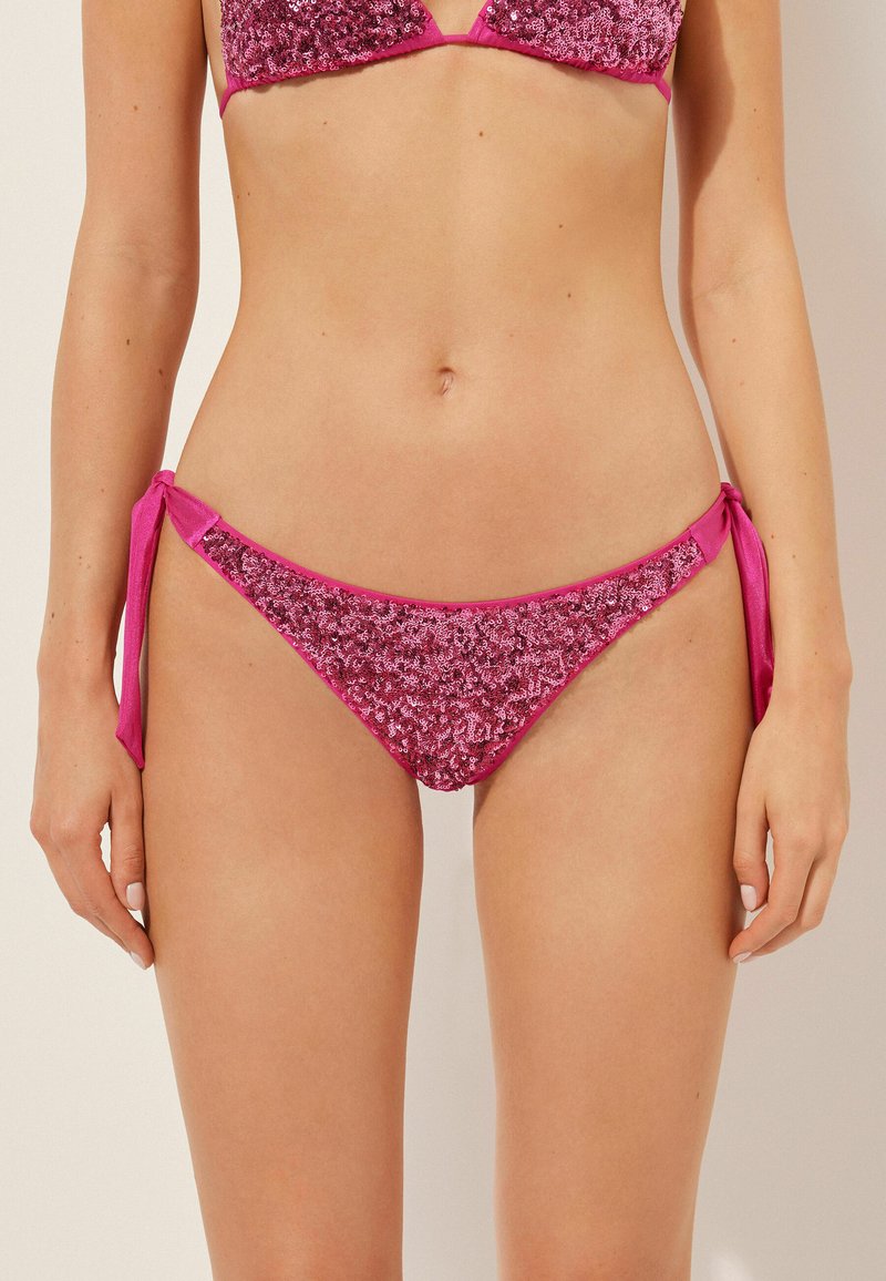 Rosa Pailletten-Bikini-Oberteil mit seitlichen Bindebändern. Glänzende Textur und kontrastierende einfarbige Akzente. Verstellbare Schleifen an den Hüften.