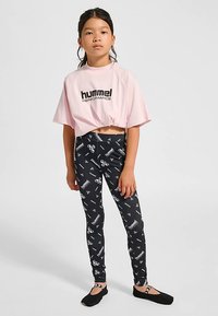 Rosa kort t-shirt med svart "hummel PERFORMANCE"-logotyp, kombinerad med svarta leggings med vita logotyper och mönster, kompletterad med svart fotbeklädnad.