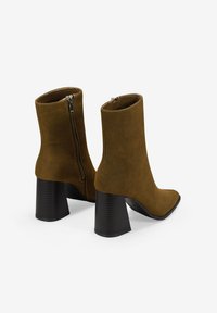 Botas de tobillo de ante sintético marrón con punta afilada y tacón grueso estriado. Cuenta con una cremallera lateral para facilitar su uso.