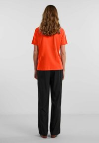Orange bomulds T-shirt med almindelig pasform, korte ærmer og rund halsudskæring, parret med sorte brede bukser.