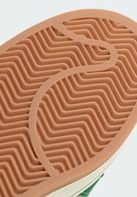 Gumowa podeszwa buta w falisty zygzakowaty wzór w jasnobrązowym kolorze, z gładkim brzegiem i teksturowanym wykończeniem wzdłuż obwodu.