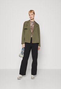Olive green jacket with a lapel, patterned top, black cargo pants, and silver sneakers. Carrying a small blue handbag.