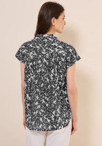 Zwart-wit gestreepte blouse met korte mouwen en kraag, met een losse pasvorm en rugplooidetail, gemaakt van lichte stof.