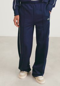 Navy blue athletic pants made of soft fabric, featuring white side stripes and a loose fit, with an embroidered logo above the left pocket.