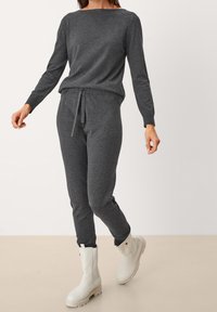 Maglione grigio a maglia con scollatura ampia, abbinato a joggers coordinati con vita regolabile. Gli stivali bianchi alla caviglia completano l'outfit.