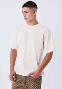 Camiseta de color crema, de manga corta y corte relajado, con un sutil diseño texturizado en la parte delantera. Tela suave, estilo minimalista.