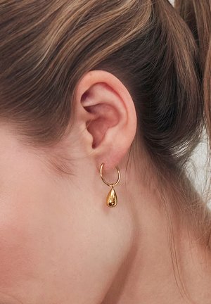 Gli orecchini a cerchio in oro presentano un pendente a goccia, una superficie liscia e una finitura lucida, appesi a un piccolo anello.