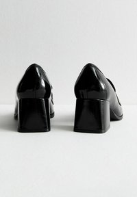 Black patent leather heels with a pointed toe and chunky block heel. Smooth texture with a glossy finish, featuring minimal detailing.