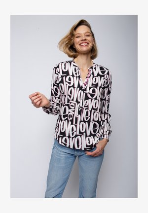 Black button-up shirt featuring large pink "love" text in various orientations. Long sleeves and relaxed fit, paired with light blue jeans.