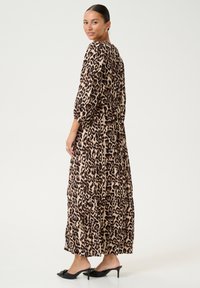 Robe maxi en tissu beige avec imprimé léopard noir, dotée de manches longues et d'une coupe décontractée. Portée avec des mules à talons noires.