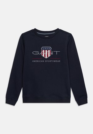 Navy blue long-sleeve sweatshirt with "GANT" logo, red and white shield emblem, "1949," and "American Sportswear" text on front.