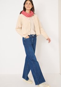 Giacca di velluto a coste beige, top beige chiaro, jeans a palazzo blu e sciarpa rosa a fantasia. Outfit casual con tessuto testurizzato e design a gamba larga.
