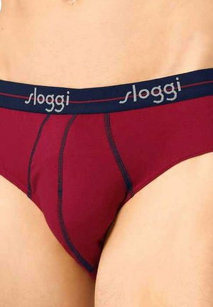 Person trägt bordeauxrote Slips mit marineblauem Bund, auf dem der Markenname "Sloggi" in hellgrauen Buchstaben steht.