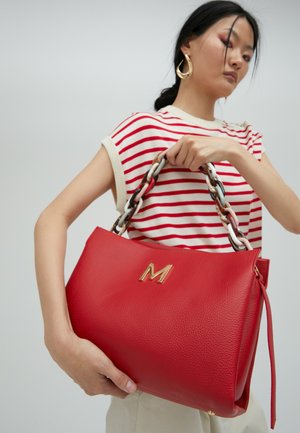 Crvena kožna torbica s teksturiranom površinom, s zlatnim logotipom "M" i višebojnim lančanim remenom.