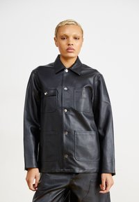 Giacca di pelle nera con colletto, due tasche frontali e bottoni a pressione argentati. Texture liscia con una finitura elegante.