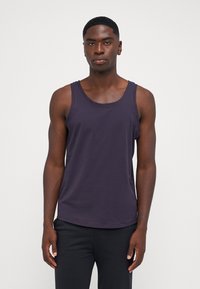 Débardeur sans manches violet foncé en tissu doux, avec un col rond et une coupe décontractée, associé à un pantalon noir.