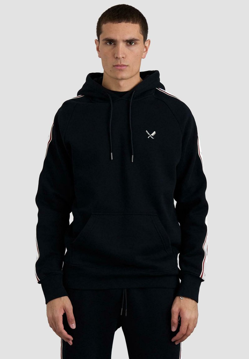 Sudadera negra con capucha, bolsillo frontal, rayas contrastantes a lo largo de las mangas y un pequeño emblema blanco en el pecho.