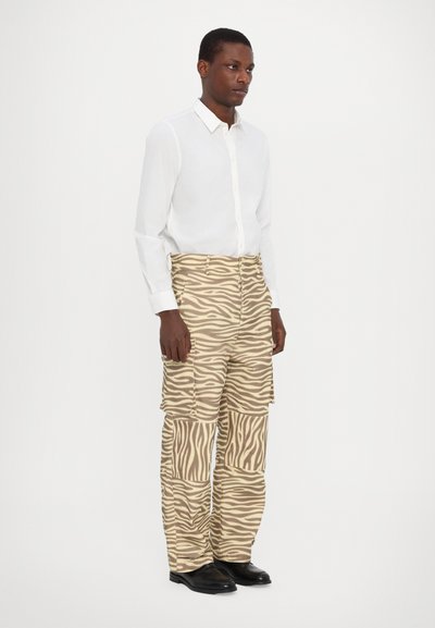 Wit lange mouwen shirt gecombineerd met beige cargobroeken met een gedurfde zebraprint en meerdere zakken, gedragen met zwarte schoenen.