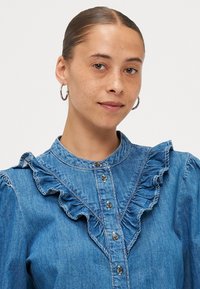 Denimskjorte med rynket krage og foran, med knappestolpe og subtile sømmer, i lys blå med en glatt tekstur.