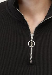 Pullover nero con zip, caratterizzato da una trama a coste. Presenta una cerniera argentata e un cursore circolare, progettato per adattarsi bene attorno al collo.