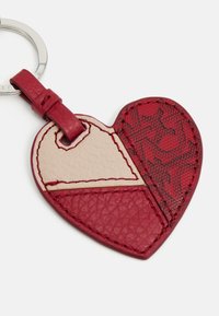 Heart-shaped keychain made from red leather, featuring a beige leather section and embossed pattern. Includes a metal key ring and strap.
