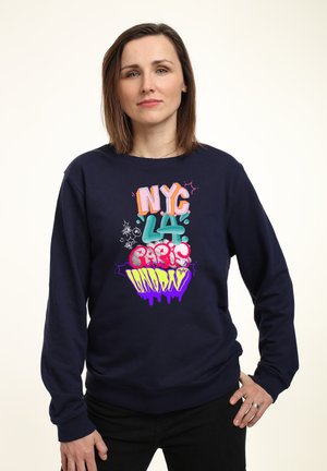 Námořnický svetr s barevným textem ve stylu graffiti, který zní "NYC LA Paříž Neděle", s uvolněným střihem a žebrovanými manžetami.