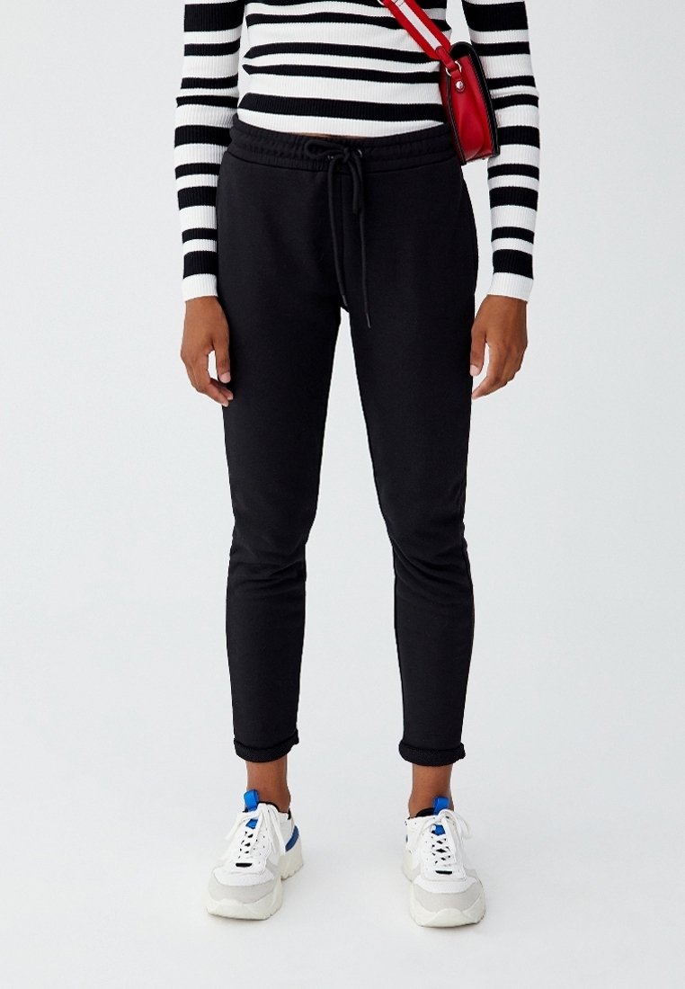 Sorte sweatpants med elastisk talje og snørredetalje, parret med hvide sneakers med blå accenter. Overdelen har sorte og hvide striber.