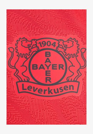 Roter Stoff mit strukturiertem Design zeigt ein rundes schwarzes Logo von Bayer Leverkusen, flankiert von zwei Löwen, und das Jahr 1904 wird deutlich angezeigt.