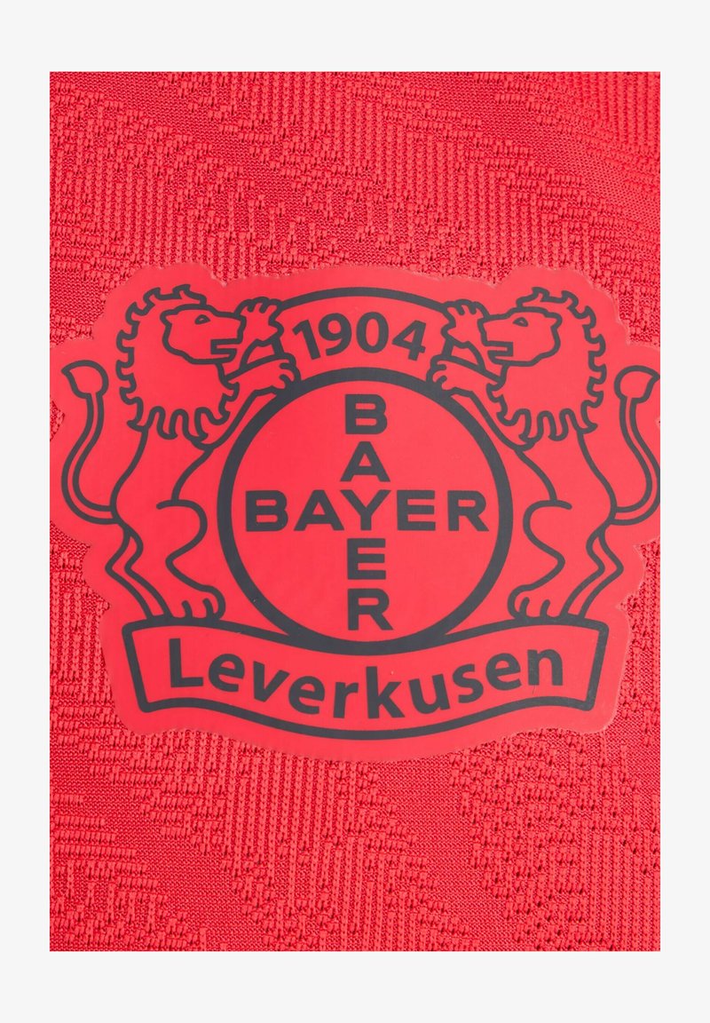 Roter Stoff mit strukturiertem Design zeigt ein rundes schwarzes Logo von Bayer Leverkusen, flankiert von zwei Löwen, und das Jahr 1904 wird deutlich angezeigt.