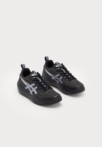 Black athletic shoes with a textured mesh upper, featuring reflective silver accents and a padded sole. Laces and heel loops for easy wear.