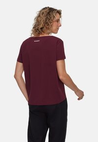 Bordowa koszulka T-shirt z krótkim rękawem o luźnym kroju, okrągłym dekolcie i logo z tyłu. Tkanina wydaje się gładka z delikatnym połyskiem.