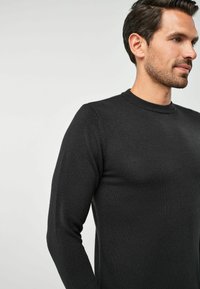Pulover negru din tricot cu guler rotund și mâneci lungi, având o textură netedă și un design ajustat. Fără modele vizibile sau detalii de metal.