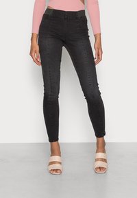 Jeans negros ajustados con una cintura alta, que cuentan con una textura suave y detalles de costura sutiles, combinados con sandalias de bloque de tacón nude.